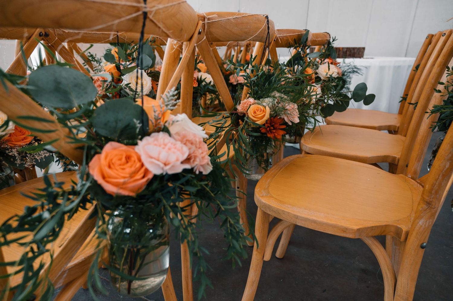 Wooden chairs decorated with peach roses and greenery for wedding ceremony.