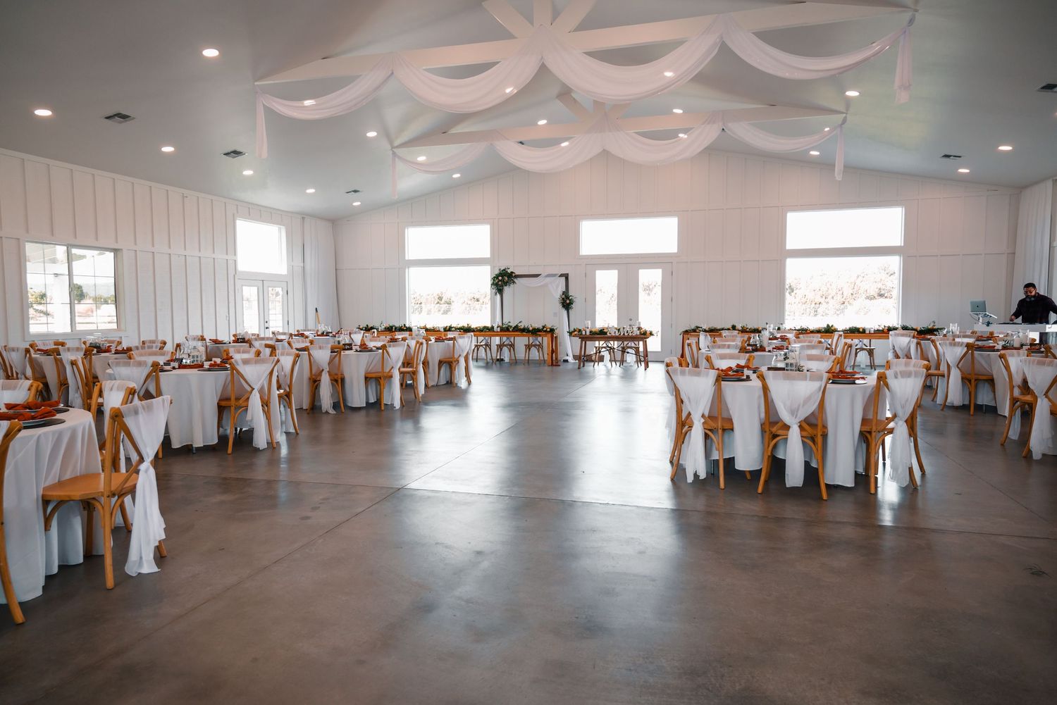 Wedding reception venue with white draping and wooden chairs arranged in rows.