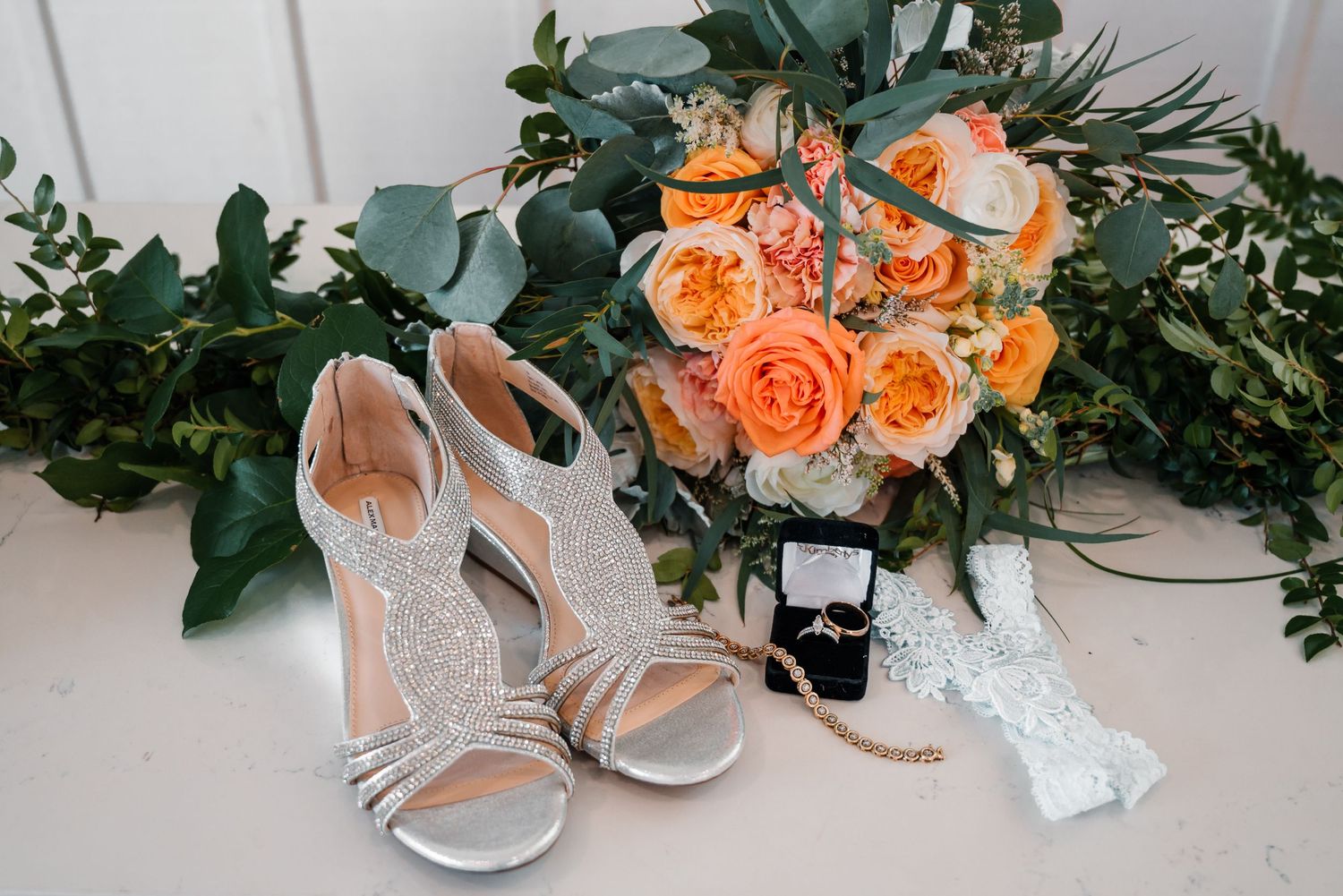 Elegant bridal shoes and accessories arranged with peach roses and eucalyptus leaves.
