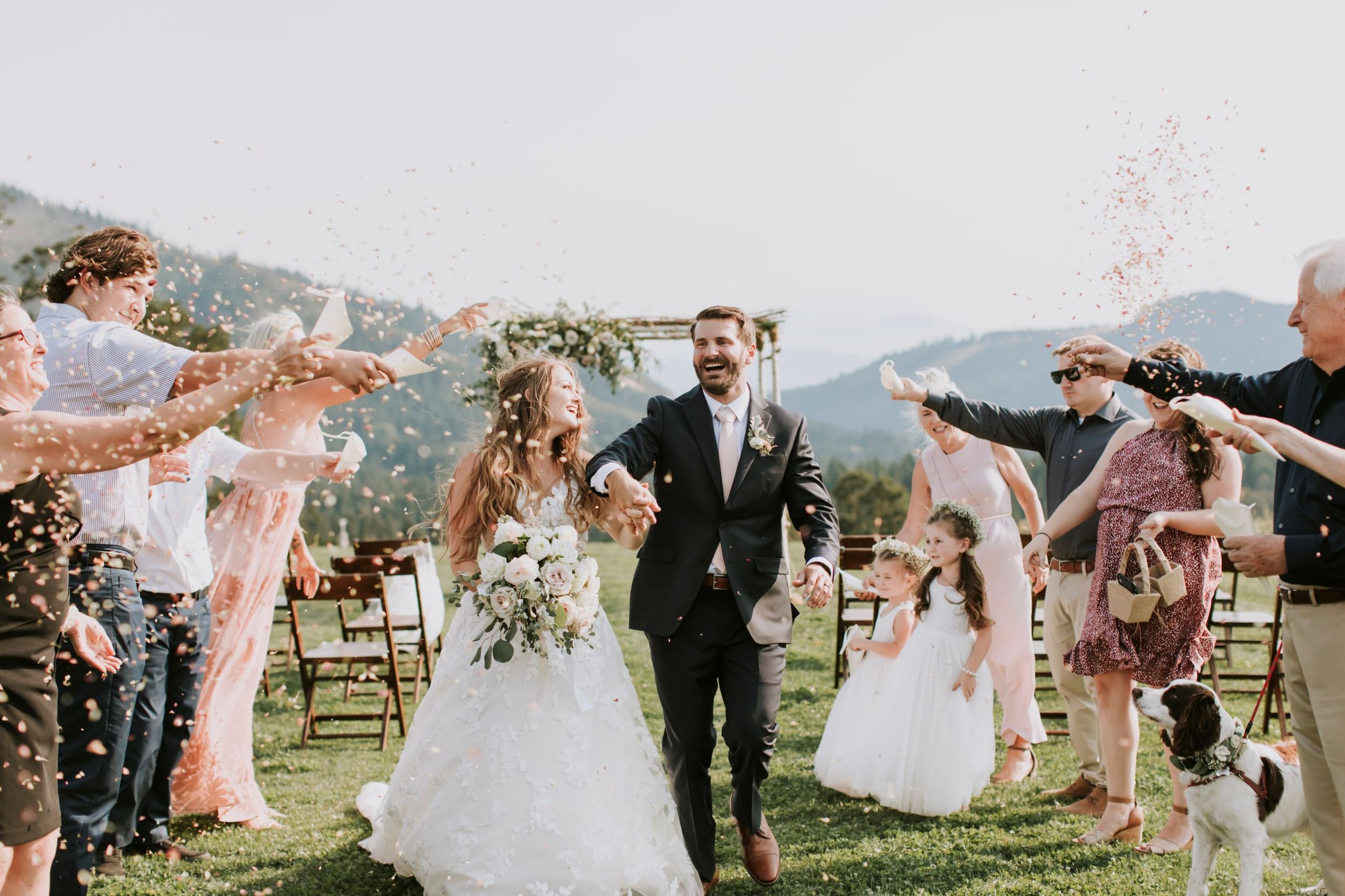 Bride and groom walking down aisle while guests stand around them cheering and throwing confetti towards them