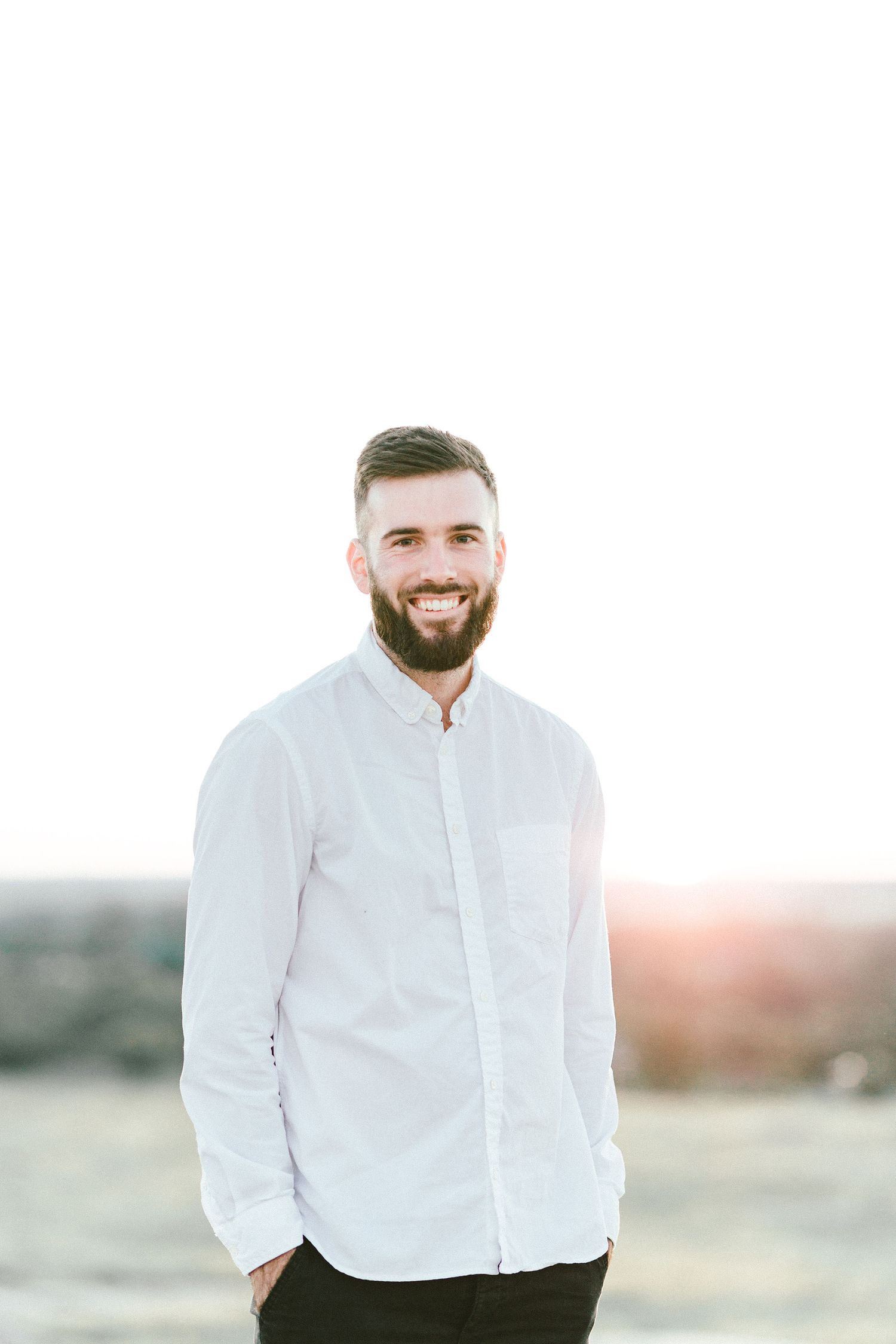 A person in a crisp white shirt smiling against a warm sunset backdrop.