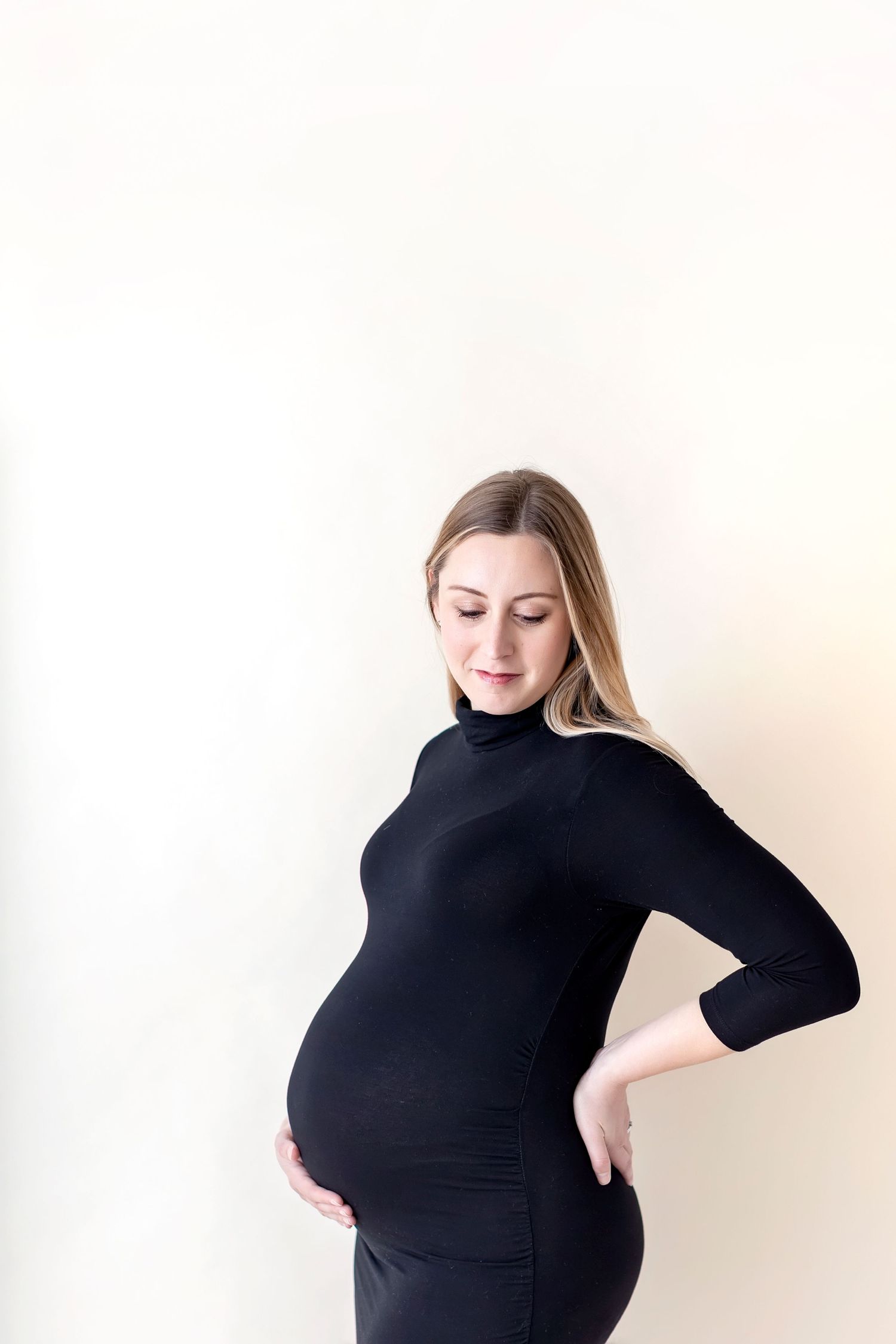 A motherhood maternity photoshoot featuring a woman in a black dress against a white background shot at Clear Lake Photo studio.