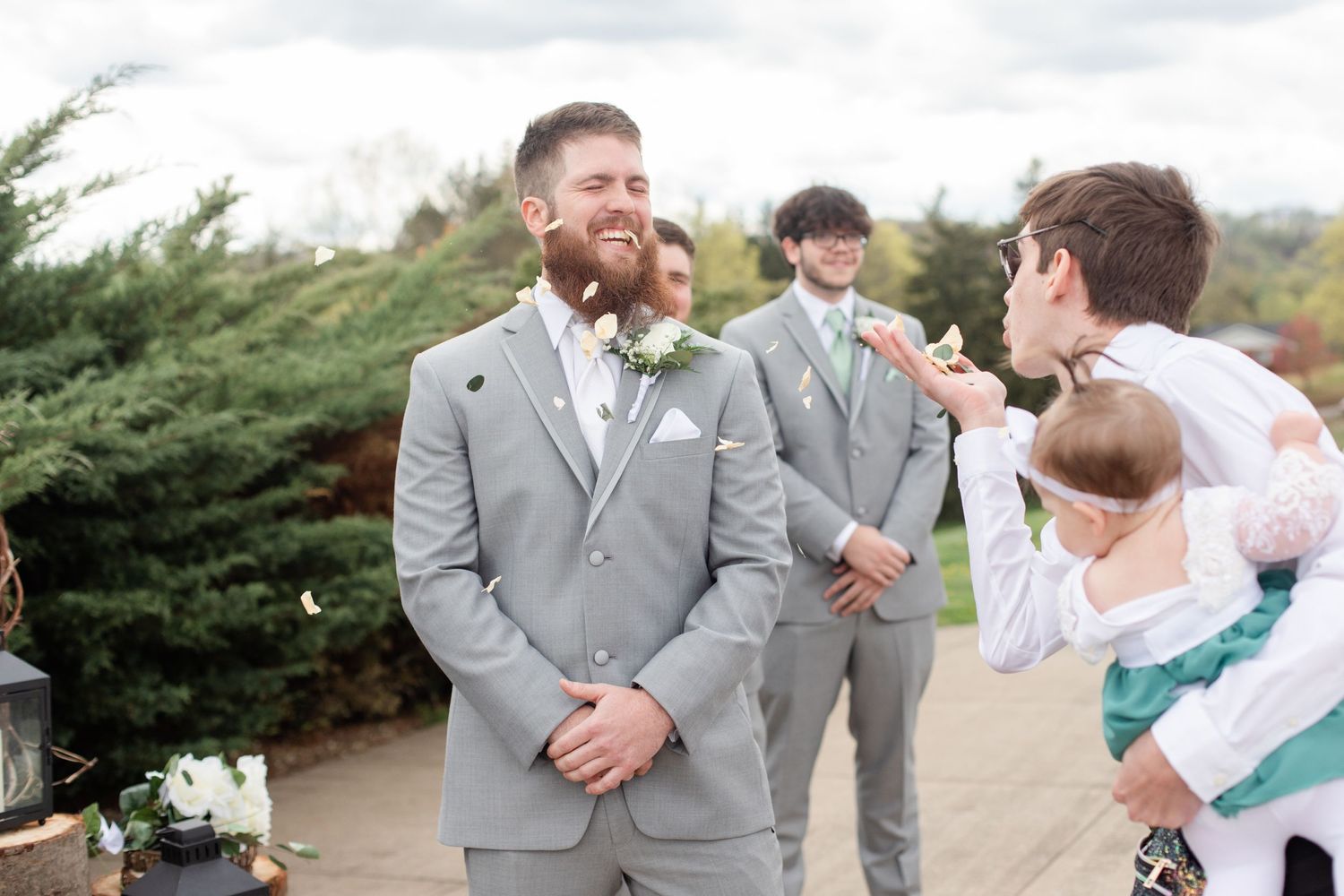Wedding party members in gray suits share laughs during outdoor photos.