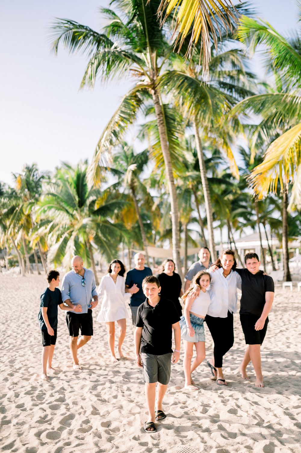 Family group poses on tropical beach with palm trees and sand.