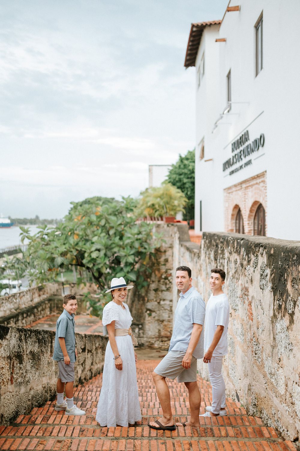 Group posing on historic stone steps with white Spanish colonial building and tropical landscape in background.