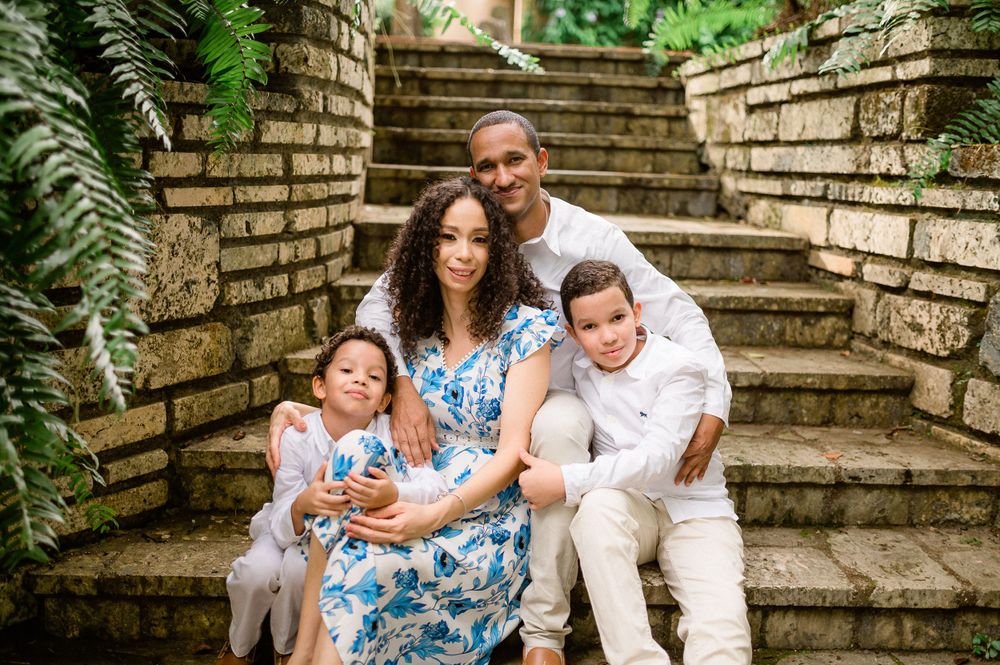 Family of four sitting together on stone steps surrounded by tropical plants.