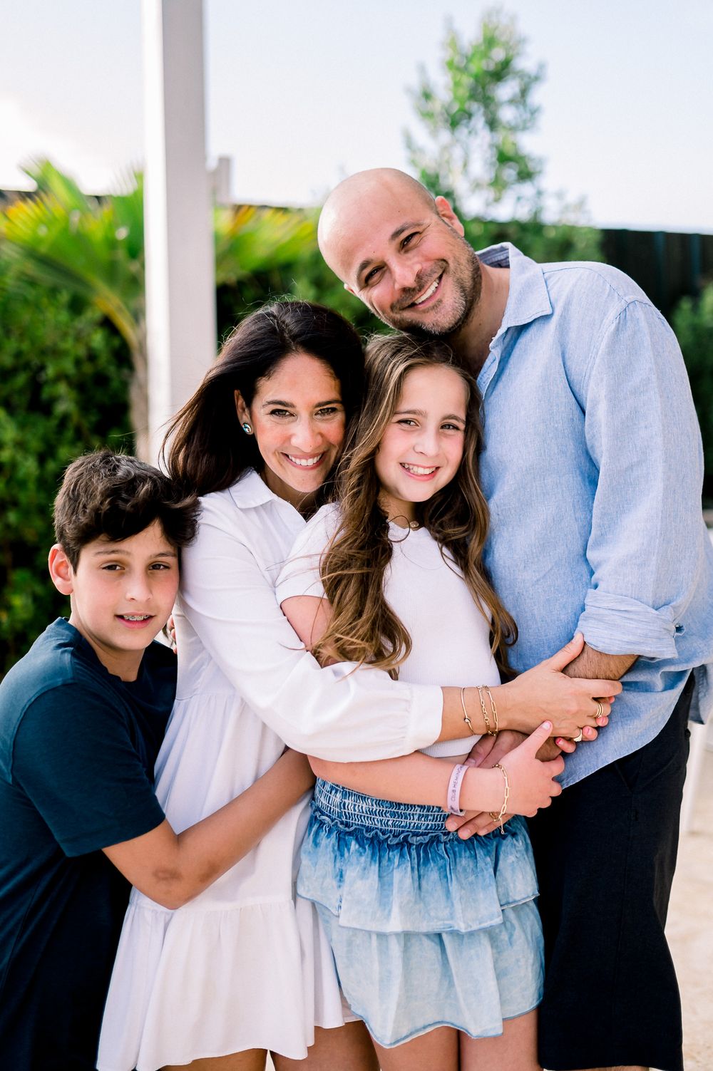 Happy family of four poses together outdoors on sunny porch.