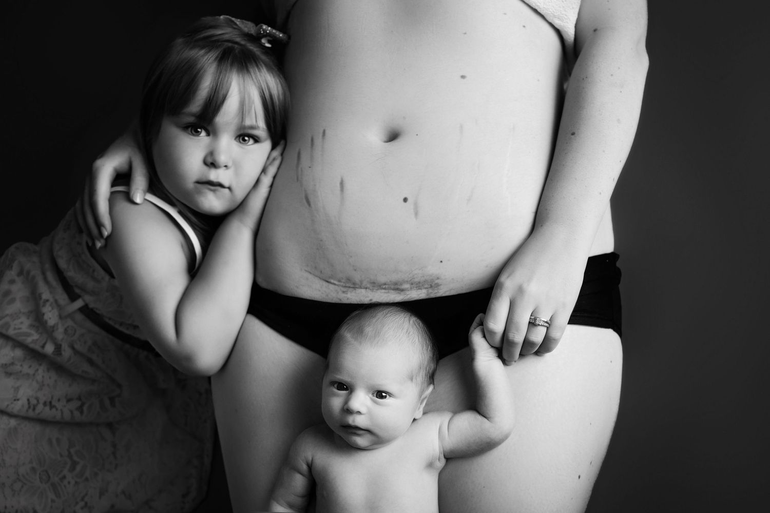 Black and white artistic portrait featuring two subjects and a pregnant belly.