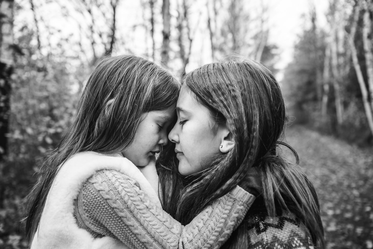 Black and white photo of indigenous sisters hugging and holding their foreheads together.