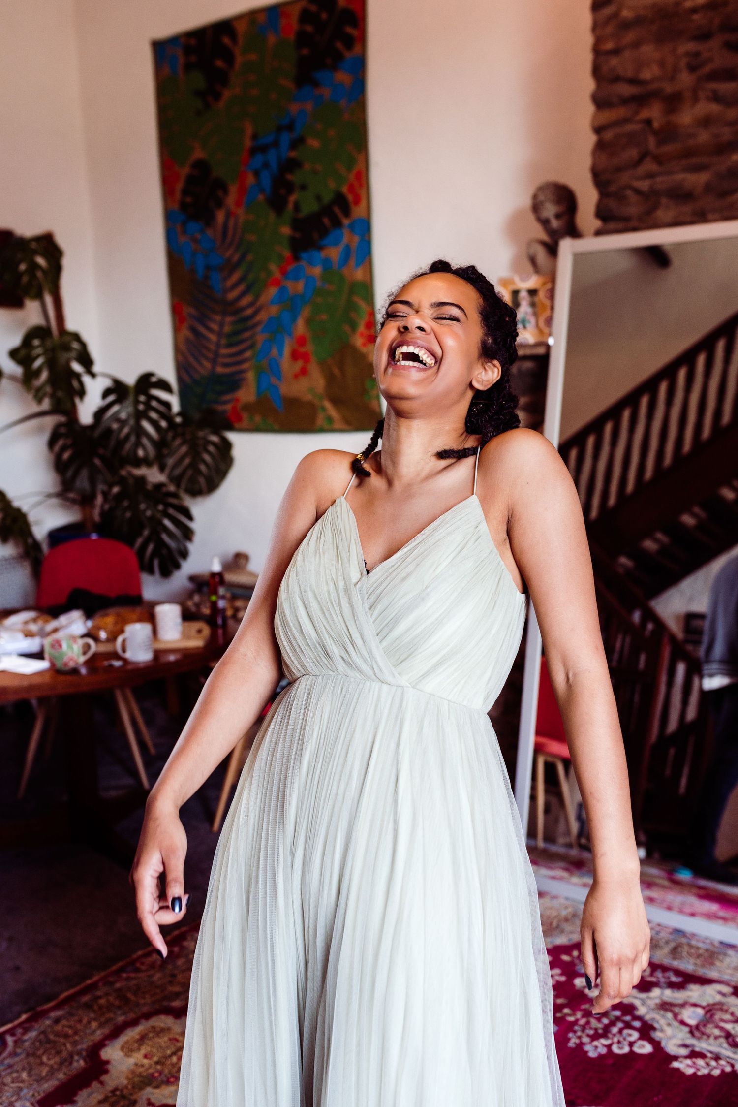 Person in flowing white dress laughing joyfully in vibrant room with colorful wall art.