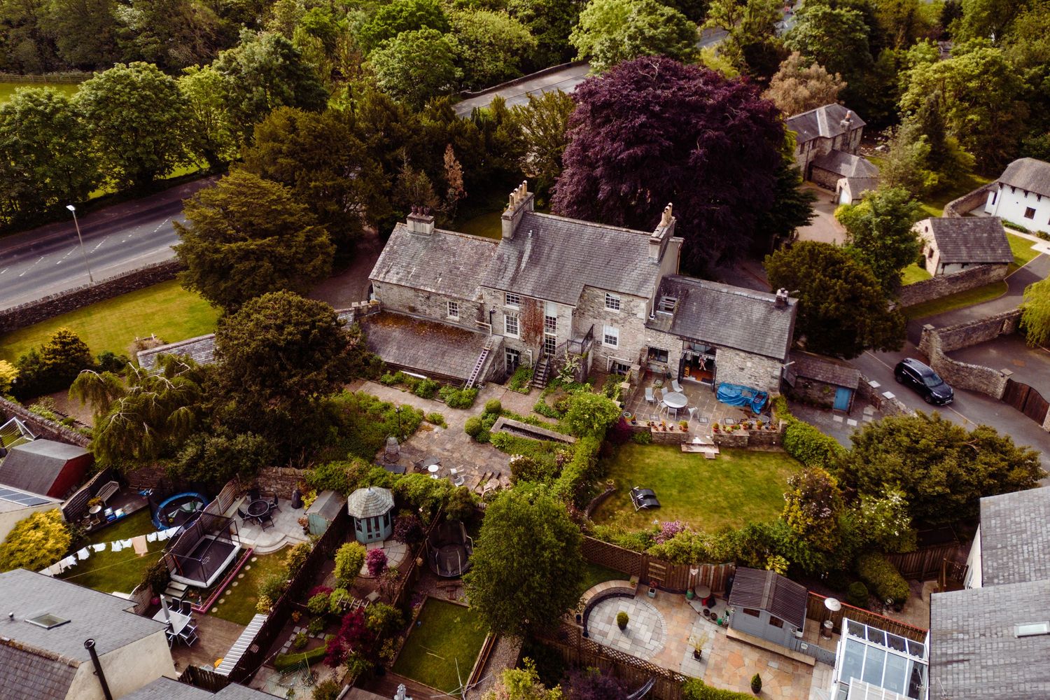 Aerial view of a stone country house with lush gardens and surrounding greenery.
