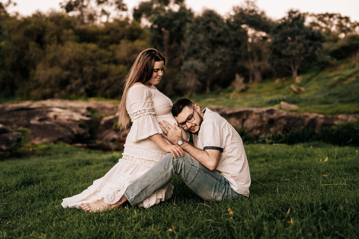 Intimate maternity photo on grass with couple sharing tender moment outdoors.