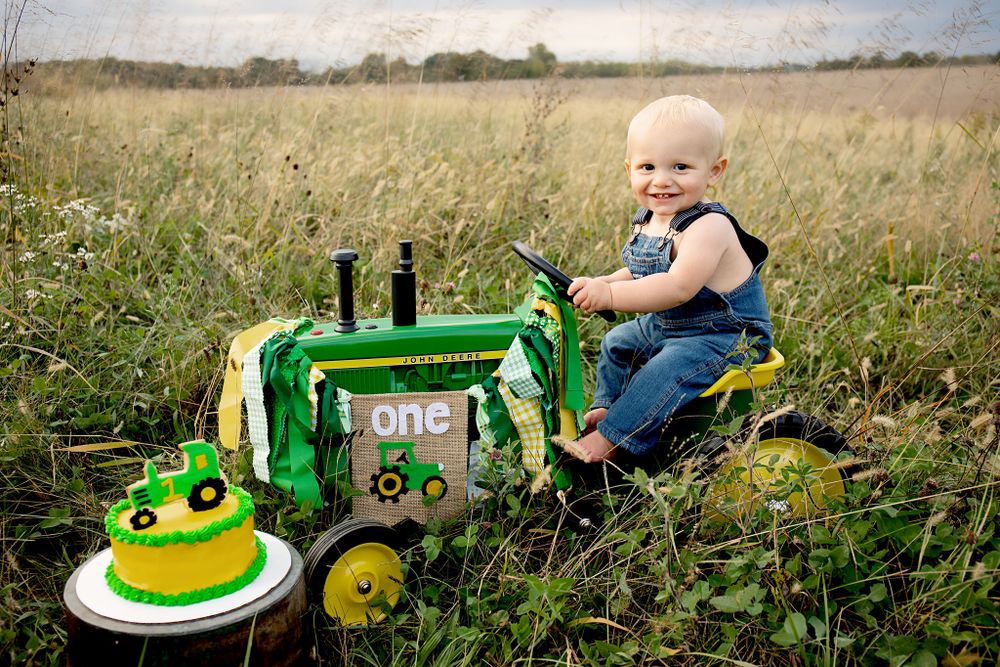 Cake smash photo with green tractor theme in sunny wildflower field.