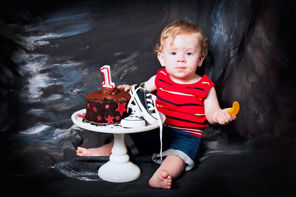 Dramatic cake smash photo with chocolate cake on white pedestal against dark background.