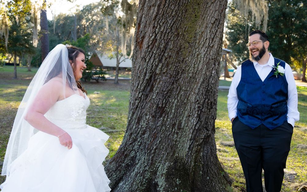 Newlyweds in a white dress and navy vest embrace warmly during their outdoor forest photo session.