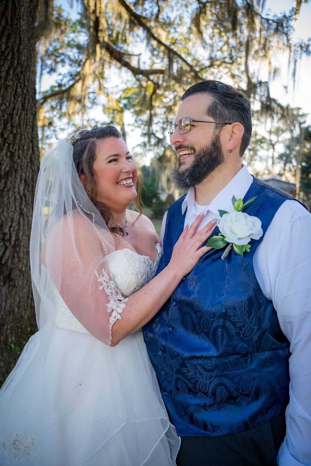 Joyful wedding couple sharing a candid laughing moment together under Spanish moss draped trees.
