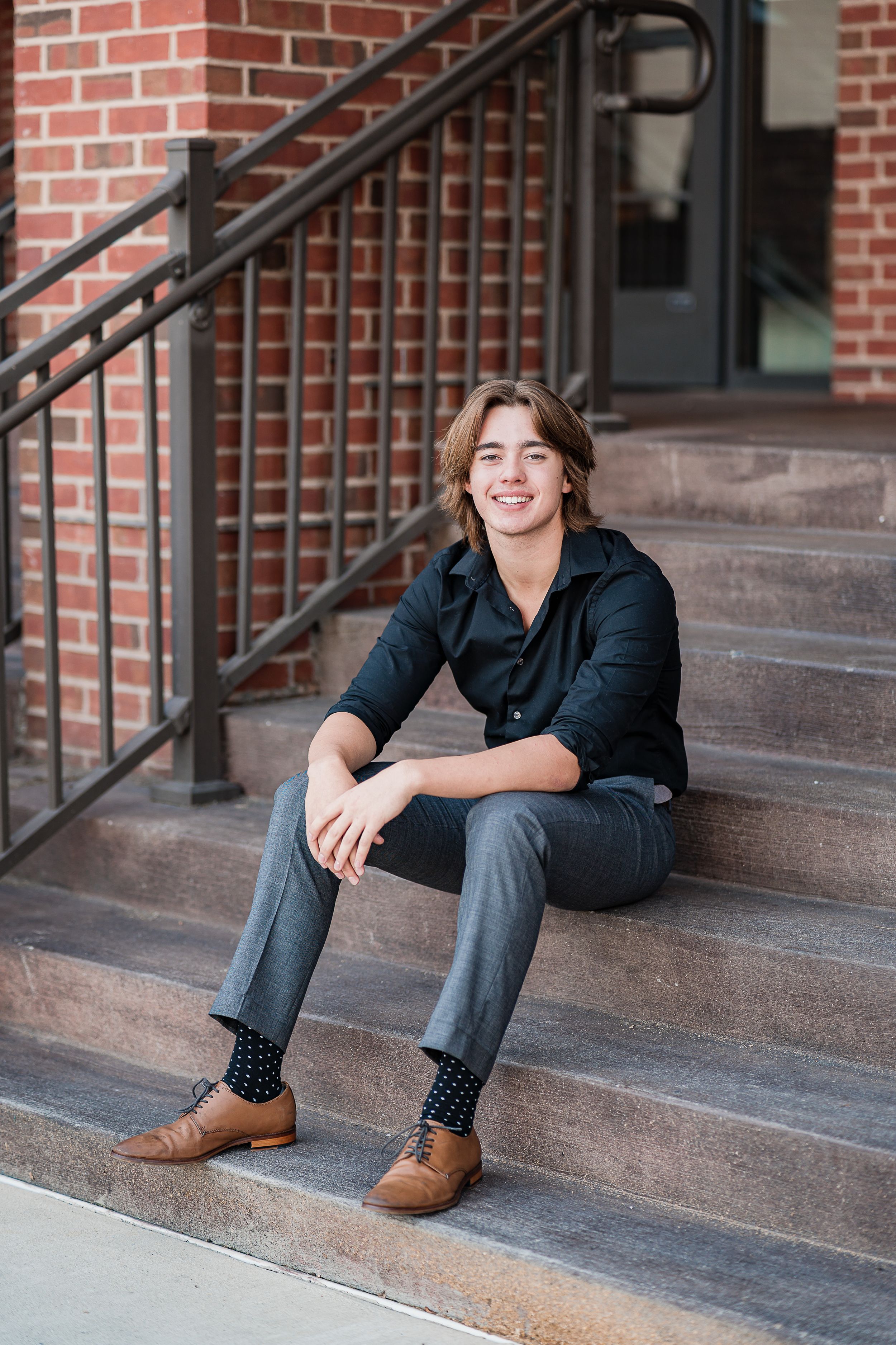 Person sitting on brick stairs wearing dark shirt and gray pants with brown shoes.