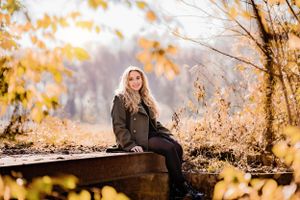 Person sitting on wooden platform surrounded by golden autumn foliage.