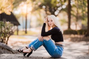 A casual outdoor portrait sitting on concrete wearing jeans and heels.