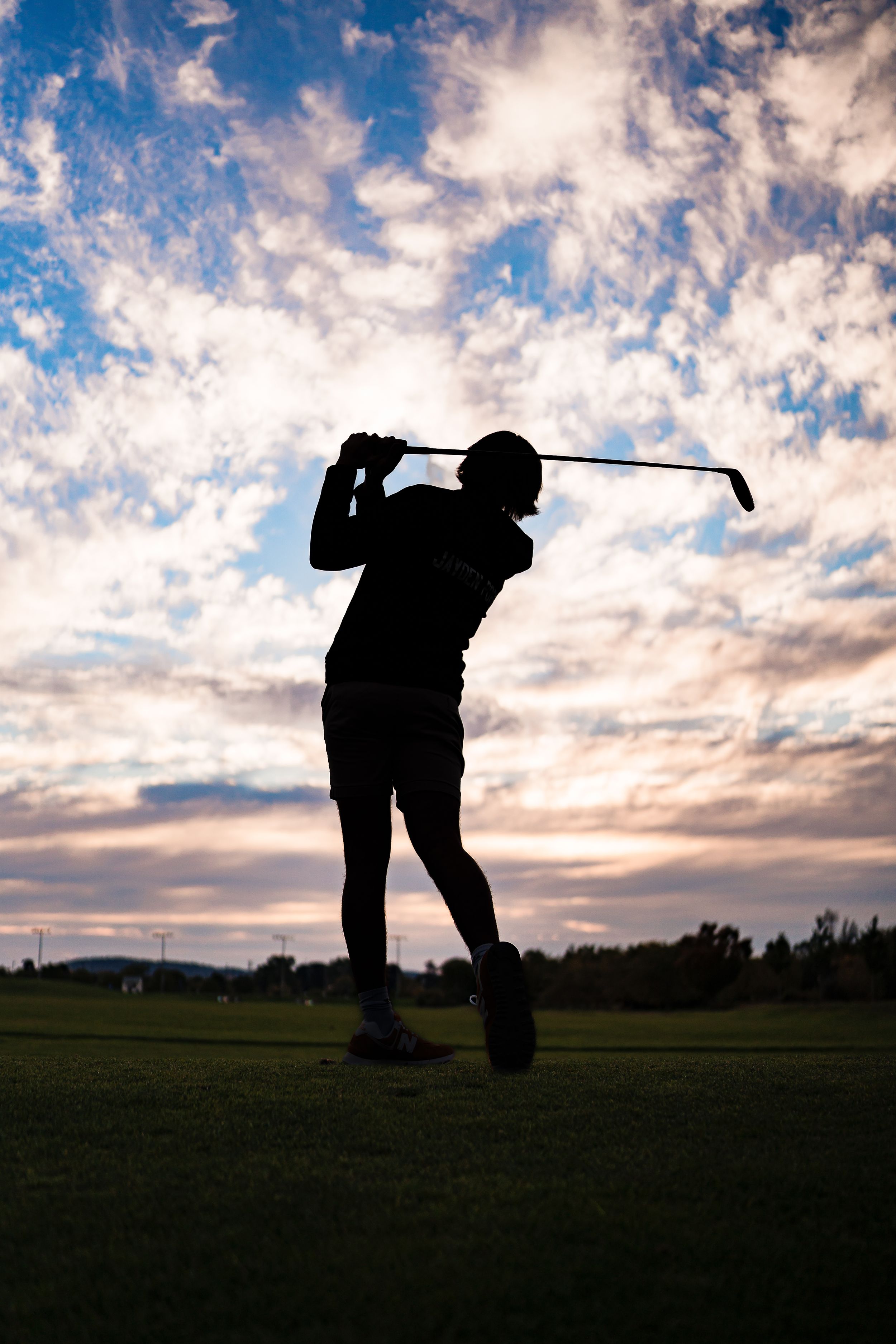 Silhouette of golfer swinging club against dramatic sunset sky with clouds.