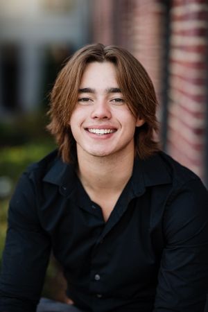 Portrait against brick building showing person in black shirt with medium-length hair.