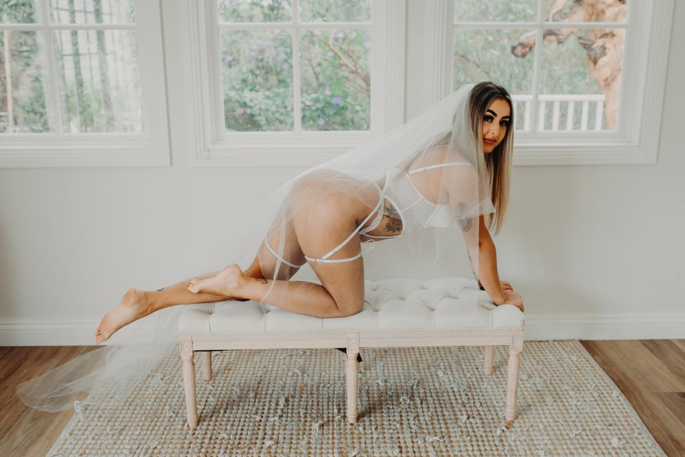 Elegant boudoir portrait featuring delicate veil draping over vintage white bench.