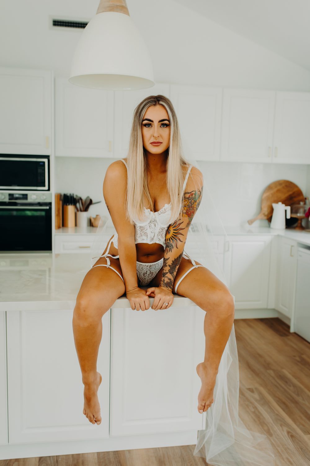 Person in white lingerie sitting casually on white kitchen counter.