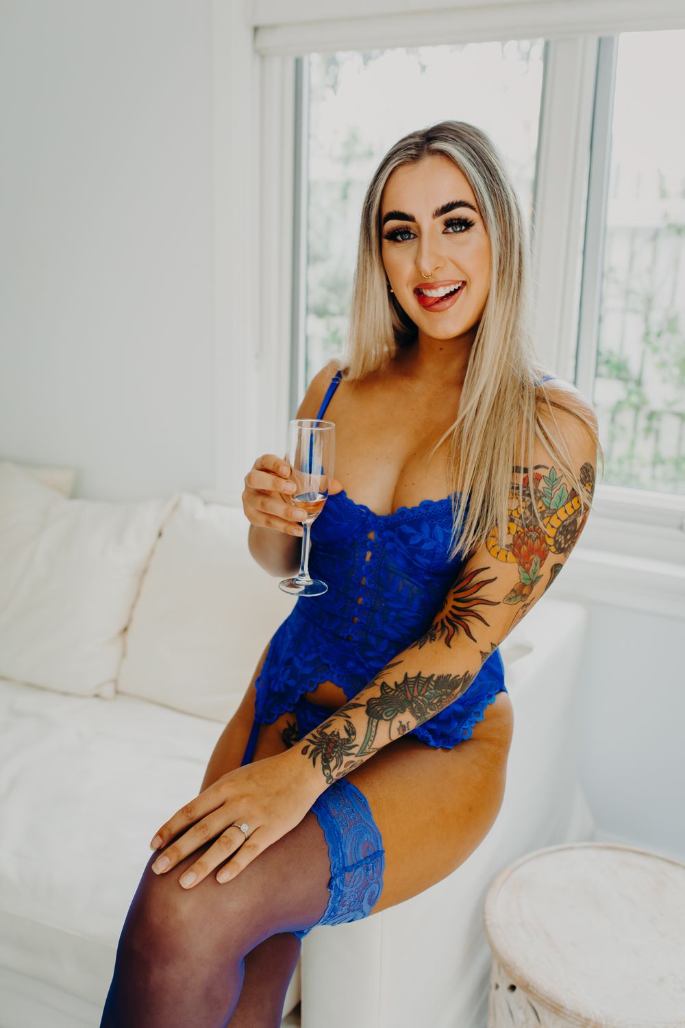 Glamour photo of woman in blue lingerie holding champagne on white couch.