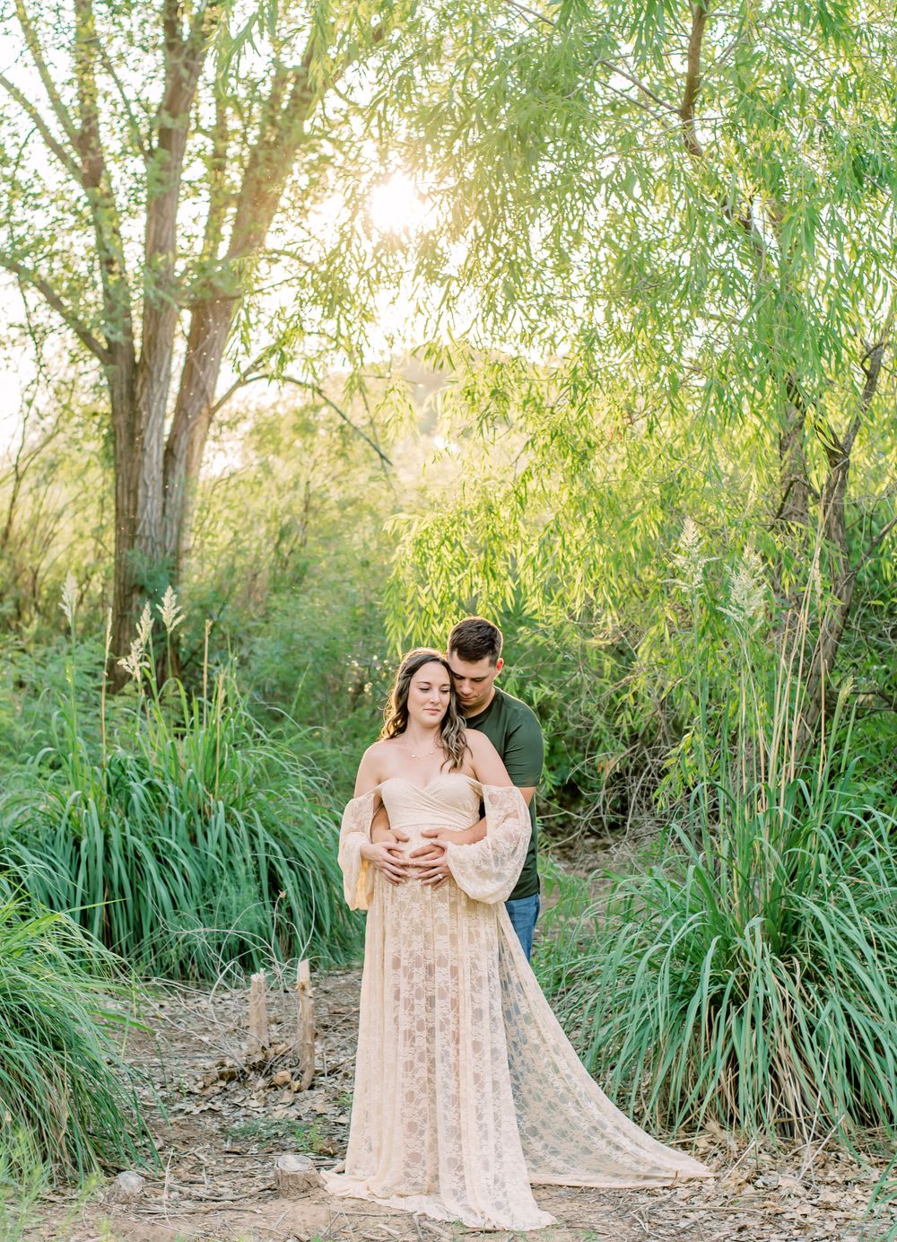 A romantic couple embraces in a dreamy willow tree setting during golden hour with the bride wearing a flowy blush gown.