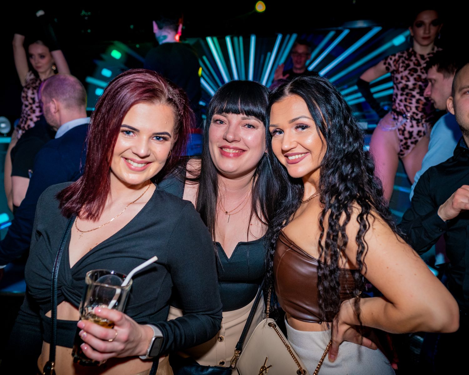 Friends posing together for a photo at a nightclub with colorful lighting in the background.