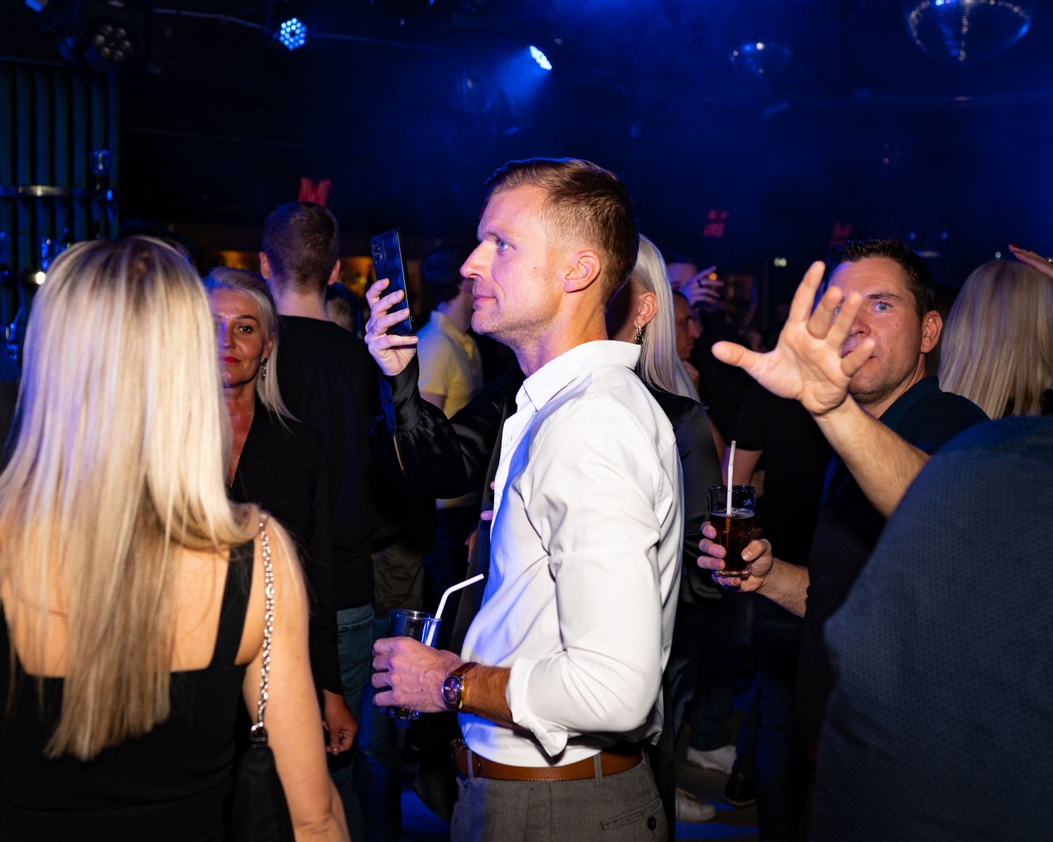Nightclub patrons socializing and drinking under blue ambient lighting.
