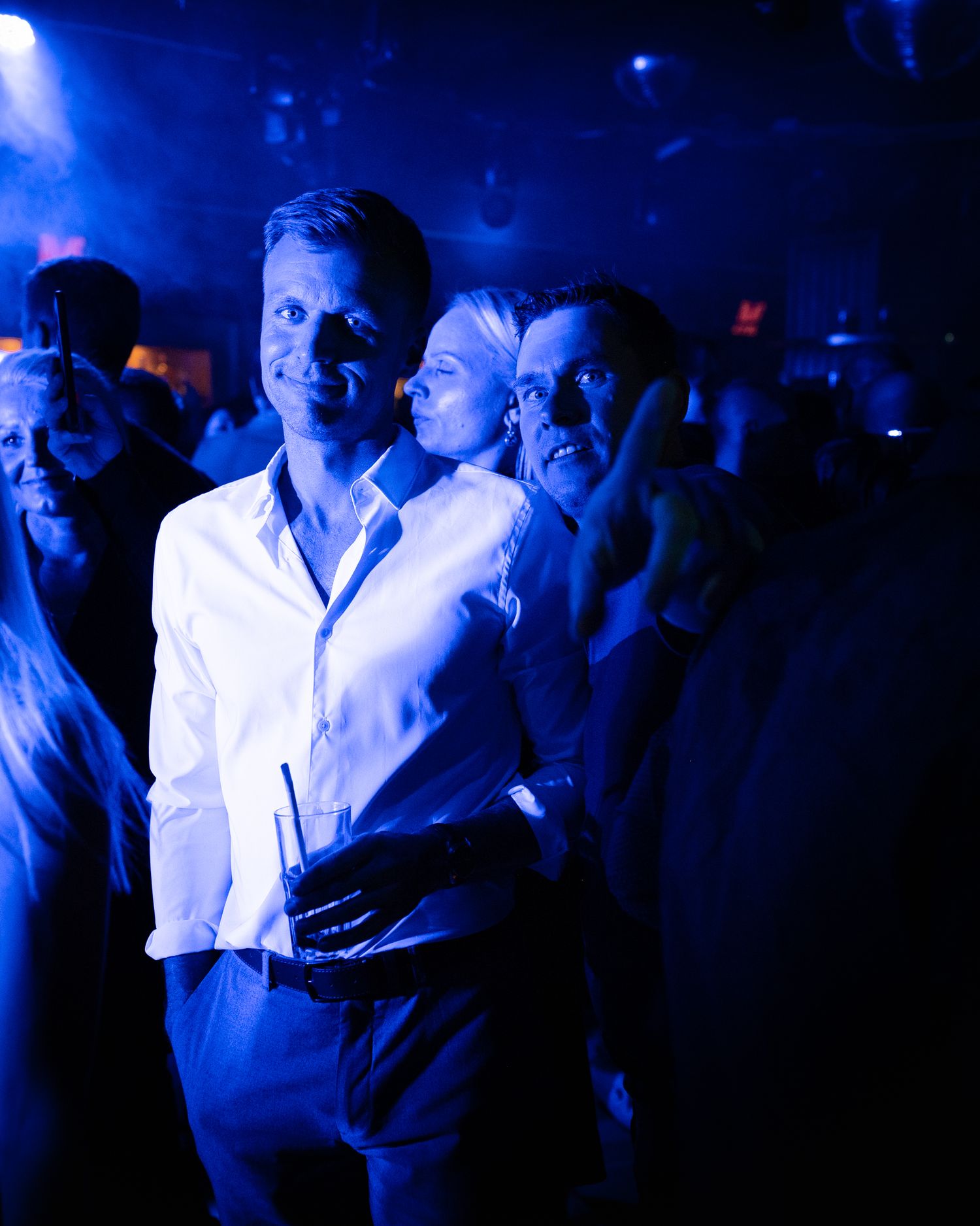 Club patrons in formal attire illuminated by blue nightclub lighting.