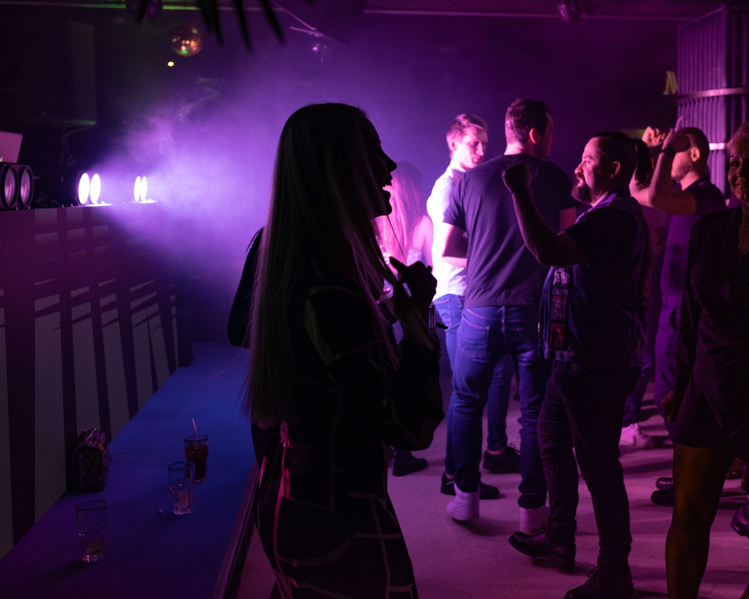Silhouettes of people gathered at a nightclub with purple lighting and fog effects.