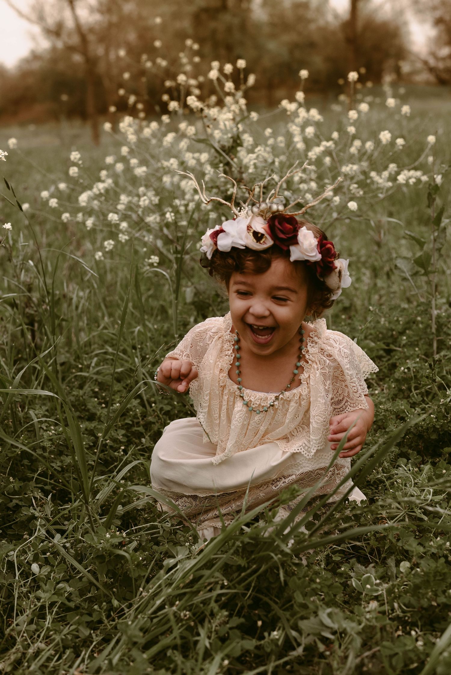 Joyful child wearing a flower crown and vintage dress laughing in a wildflower meadow.