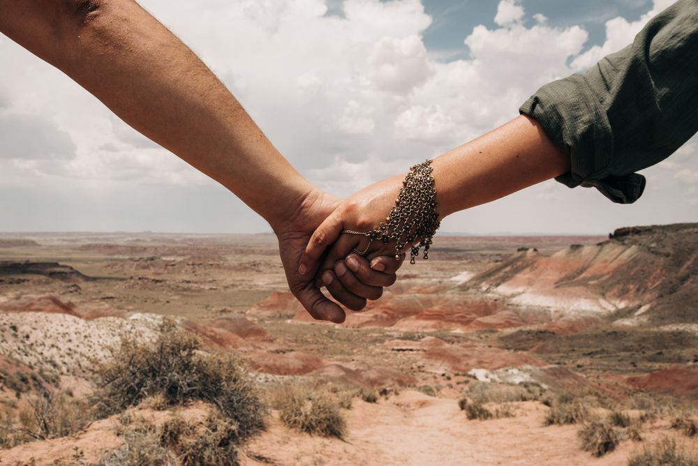 Two hands clasped together against desert canyon landscape backdrop.
