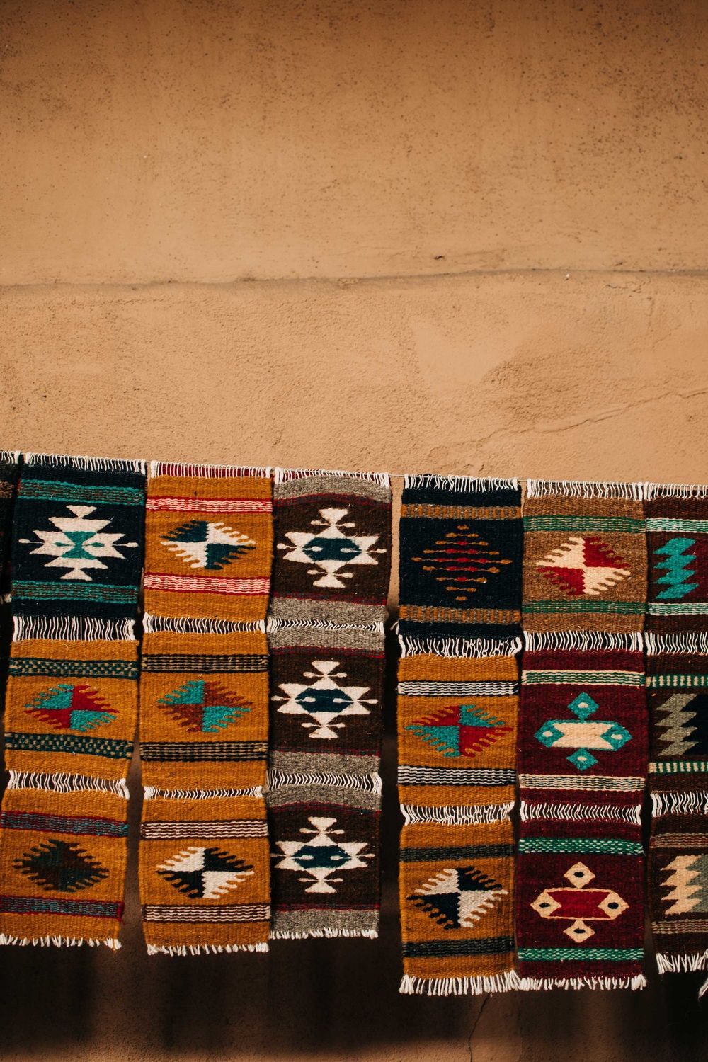 Colorful southwestern style rugs with geometric patterns displayed against an adobe wall.