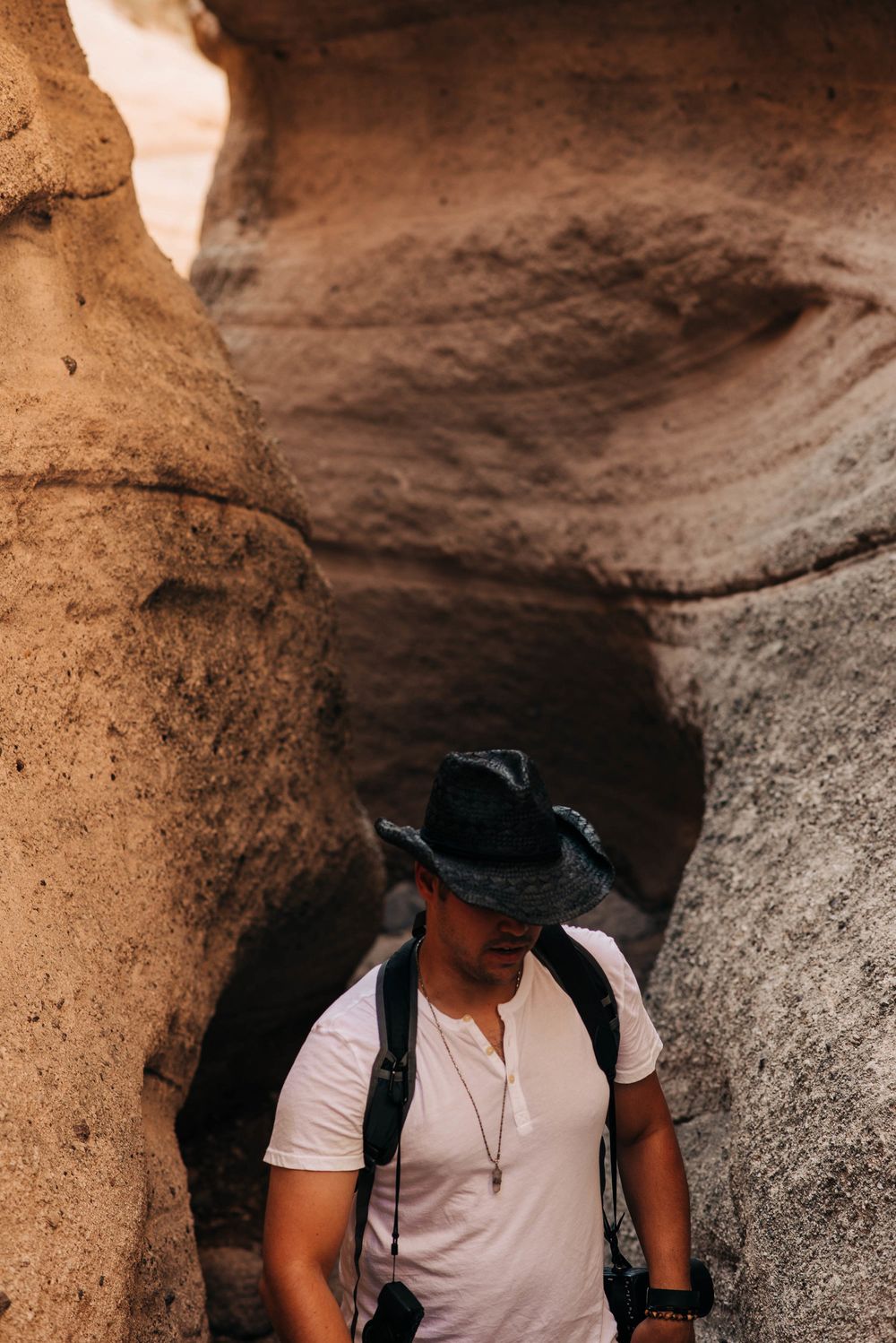 Explorer in a wide-brimmed hat navigates through narrow sandstone canyon formations.