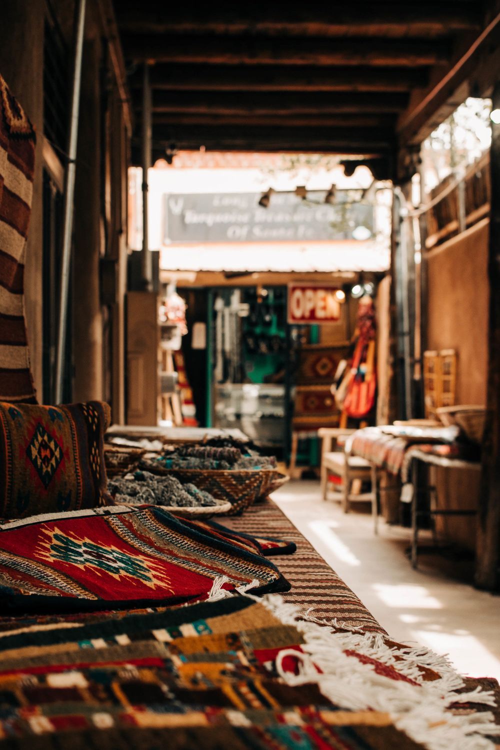 Market corridor displaying colorful woven rugs and textiles under wooden beams.