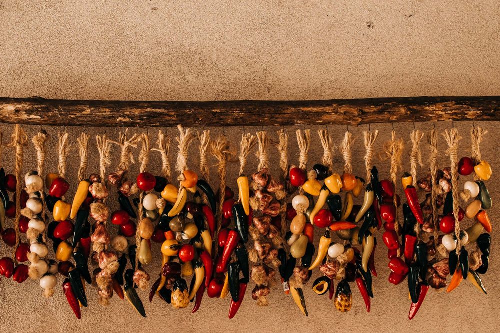 Row of colorful dried chili pepper ristras hanging against an adobe wall.