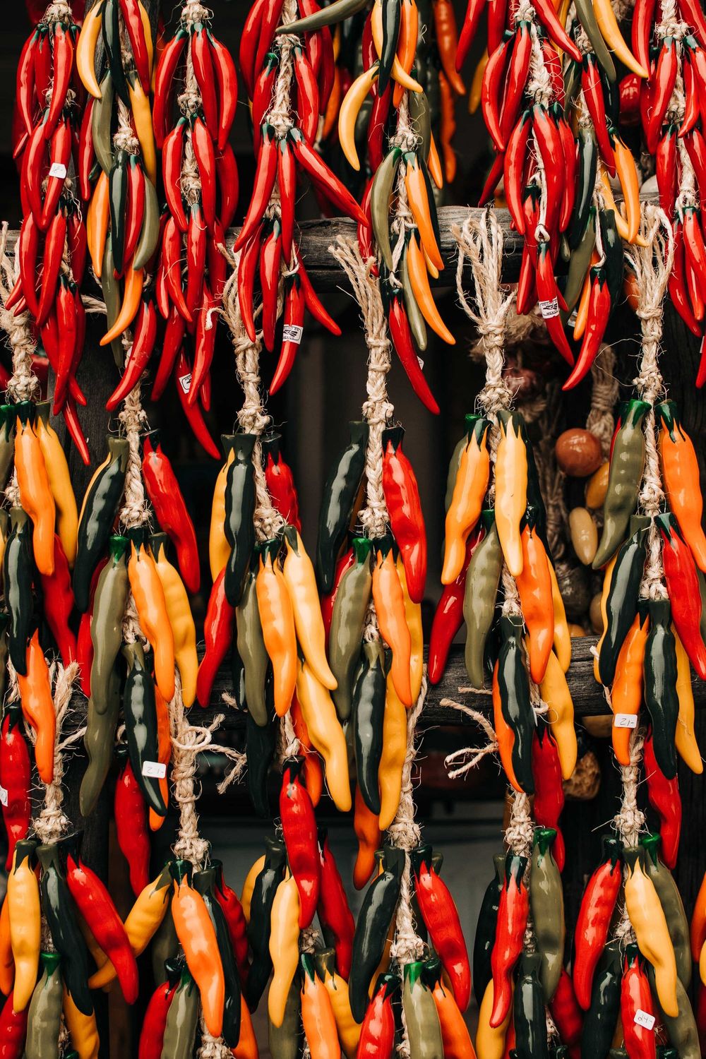 Colorful red and orange chili peppers hanging to dry in bundles against a dark background.