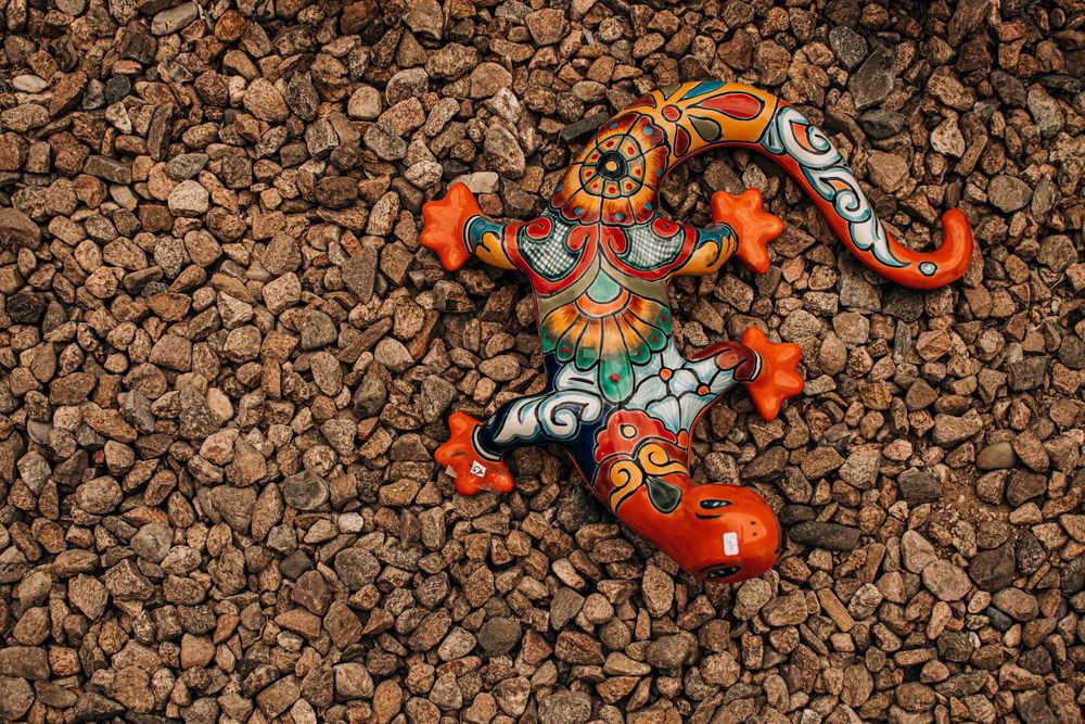 Decorative ceramic gecko with orange and turquoise patterns on gravel background.