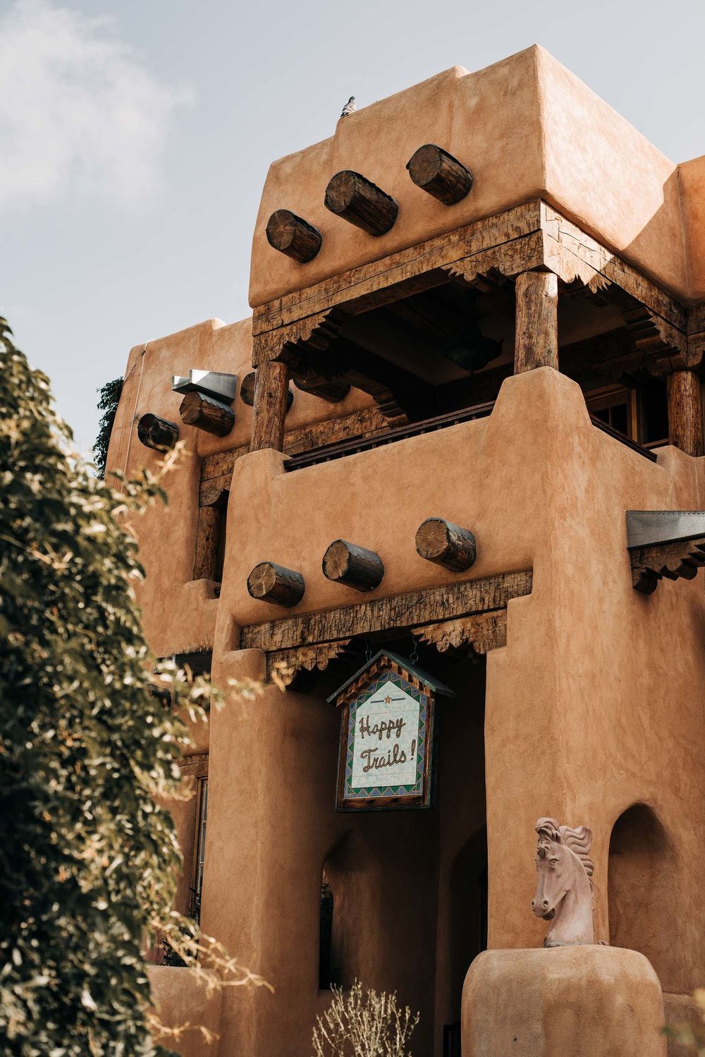 Adobe-style building with wooden beams and a 'Happy Trails' sign in Santa Fe architecture.