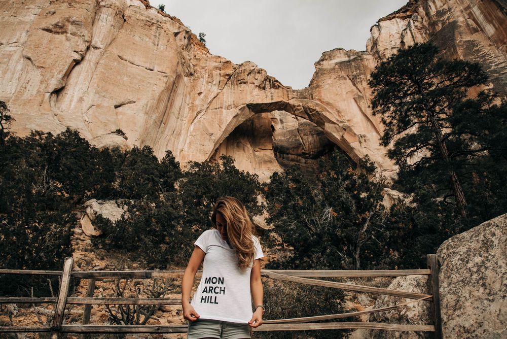 Tourist overlooking natural stone arch formation in mountainous landscape.