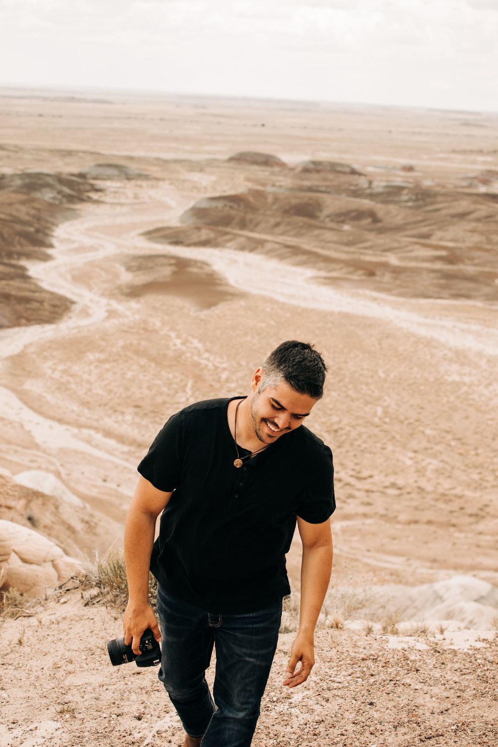 Photographer hiking desert overlook carrying camera equipment.