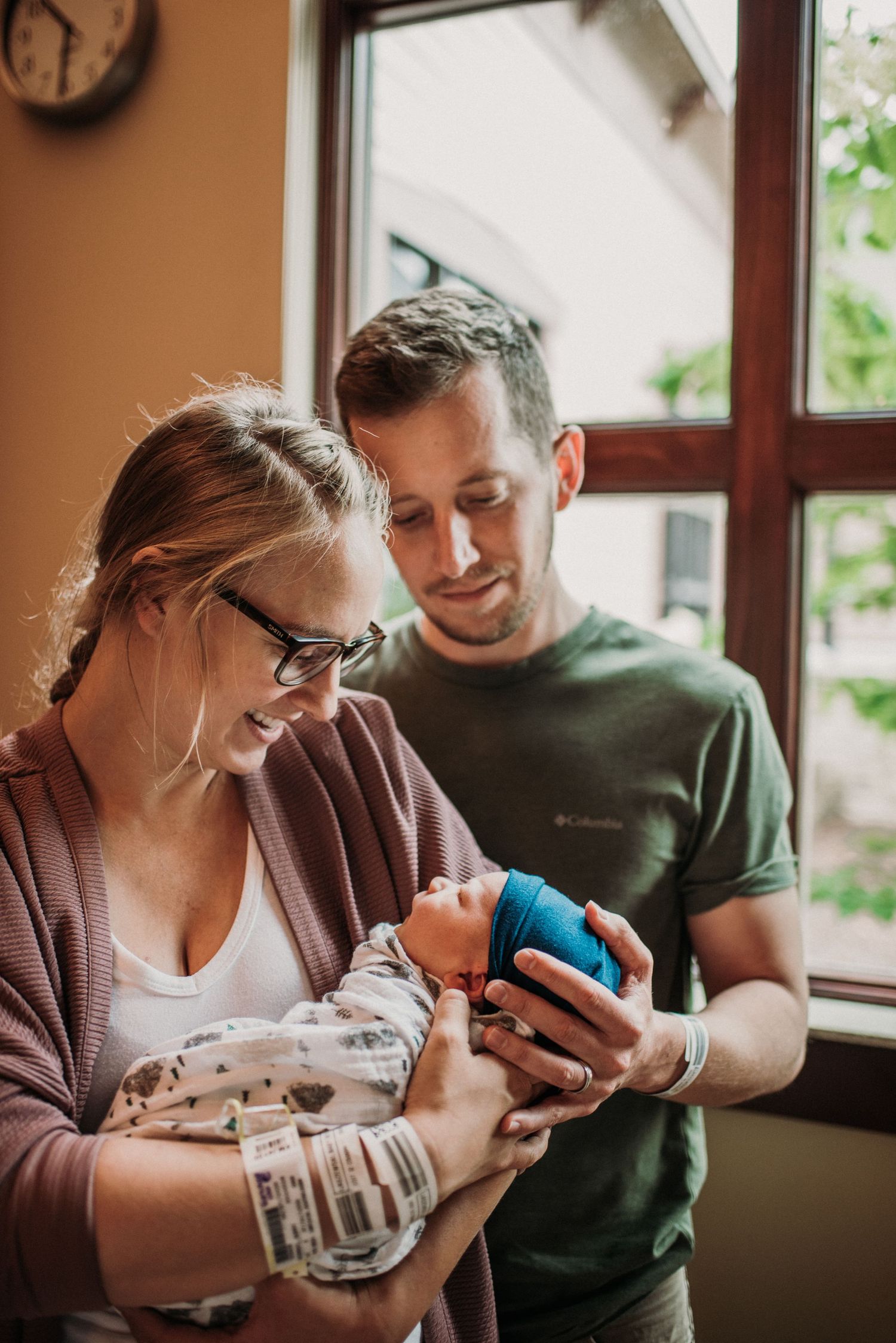 A tender moment between new parents as they hold their newborn baby by a window.