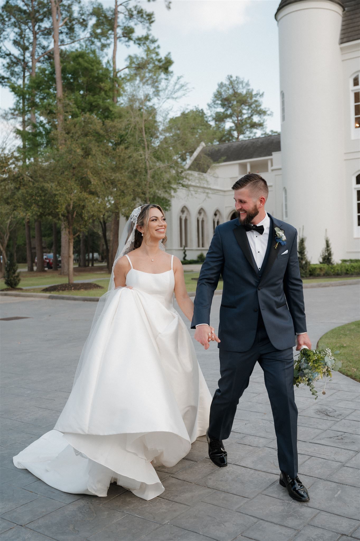 Couple walks hand in hand outside white church building with gothic architecture.