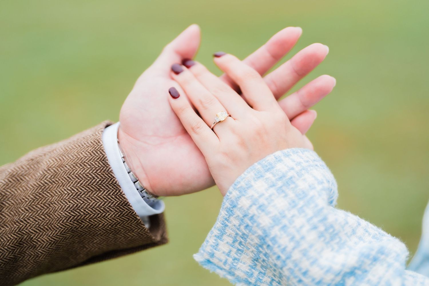 Two hands tenderly touch in an intimate moment against a blurred green background.