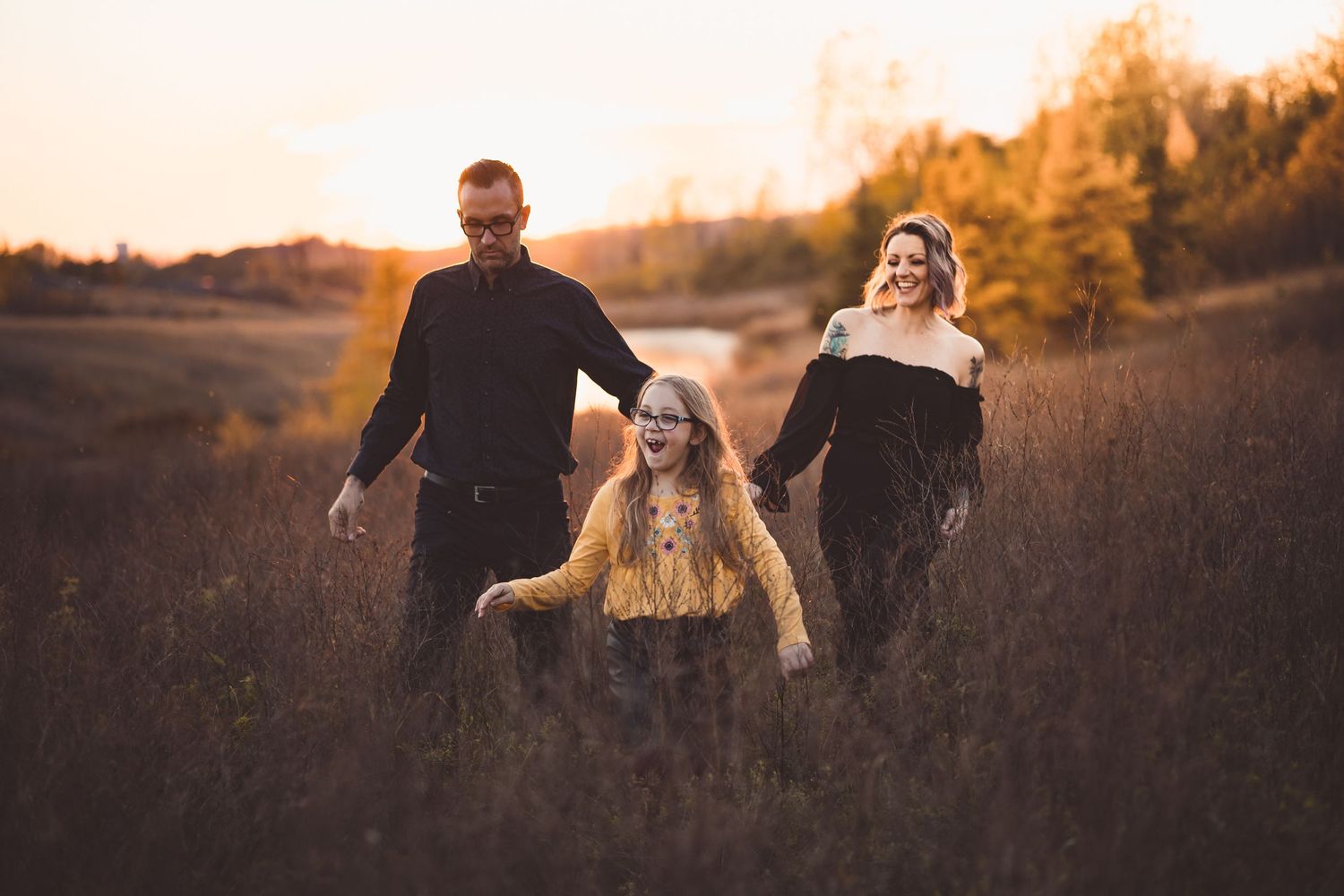 Couple walks through golden field during sunset photoshoot with dramatic lighting.