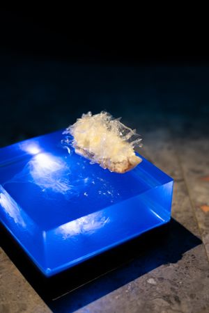 A transparent blue resin cube with crystalline structures perched on top glows against a dark background.