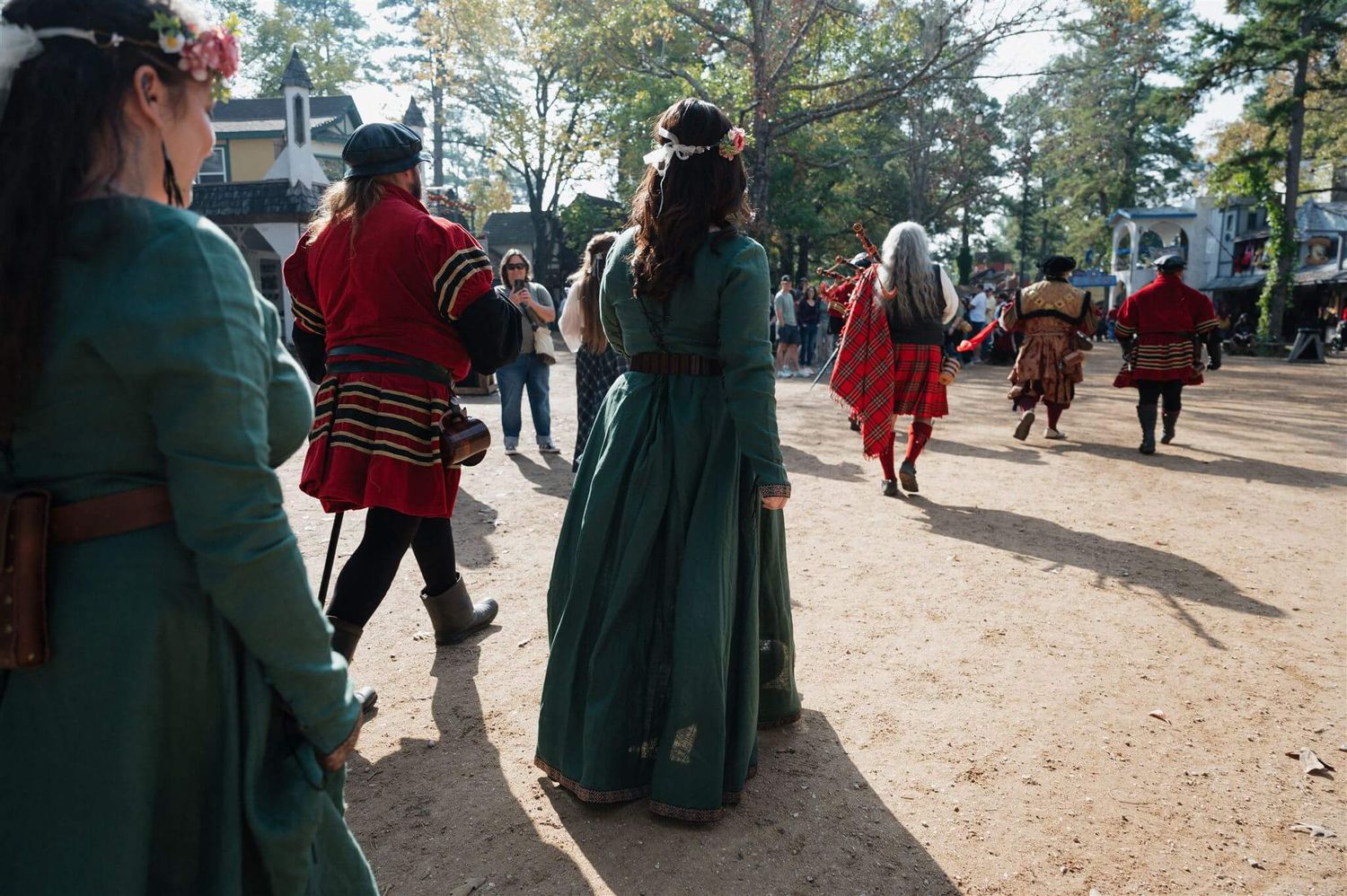 Performers in medieval costumes gather on a dirt path at a renaissance faire.